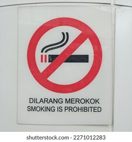 A symbol of smoking is prohibited, "Dilarang merokok" in Malay language on the white wall. - Shutterstock ID 2271012283