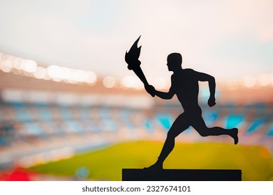 Symbol of Unity: Silhouette of Athlete Carrying the Torch Relay against the Modern Track and Field Stadium. A Captivating Photo for the Summer Game  in Paris - Powered by Shutterstock