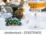 The symbol of the year is a green snake, a glass of champagne, Christmas tree branches and Christmas decorations on a gray background. The concept of Merry Christmas and New Year 2025.