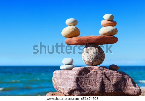 Symbolic scales of stones against the background\
of the sea and blue sky. Concept of harmony and balance. Pros and\
cons concept.