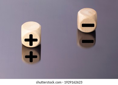 Symbols of black color plus and minus on wooden cubes on a mirror background.