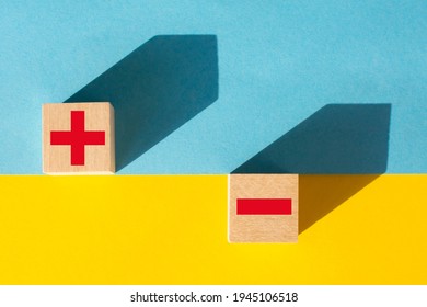 Symbols of red color plus and minus on wooden cubes on a yellow and blue background - Shutterstock ID 1945106518
