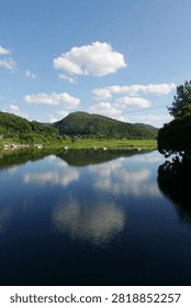 Symmetric reflection of green mountain and white clouds on calm river