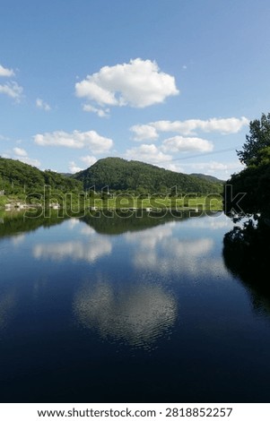 Symmetric reflection of green mountain and white clouds on calm river