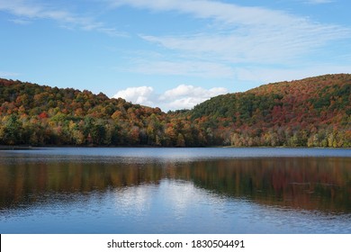 Symmetrical hills covered with coniferous and deciduous autumn trees by the lake, bright colors, blue sky, sunny day, Quebec, Canada