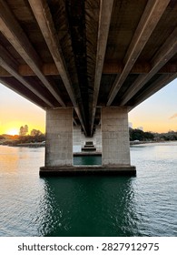 Symmetrical low angle perspective underneath a concrete highway bridge spanning a river channel at sunset.