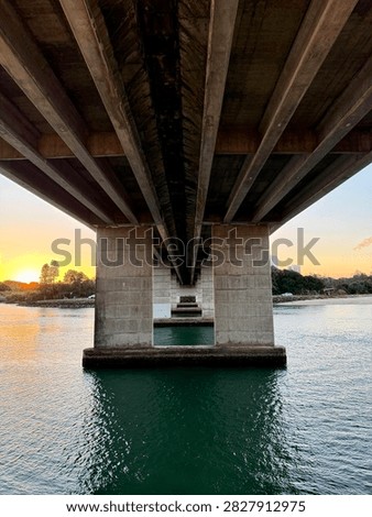 Symmetrical low angle perspective underneath a concrete highway bridge spanning a river channel at sunset.