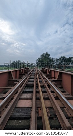 Symmetrical low angle perspective view of a railway track over an iron bridge girder under a cloudy sky, vanishing point.