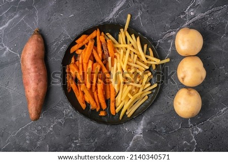 Symmetrical mix of sweet potato fries, French fries and raw vegetables on a dark background, top view
