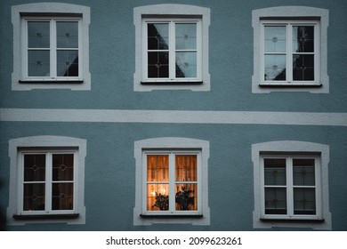 A Symmetrical Row Of Windows Of A Blue House With One Window Lit Up From The Inside