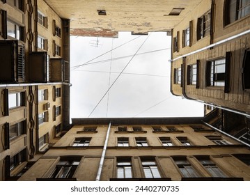 A symmetrical view of a building's courtyard with architectural details, looking up towards. Dark inner courtyard perspective, an old living houses in Saint-Petersburg, Russia - Powered by Shutterstock