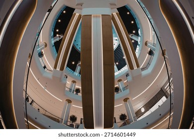 A symmetrical view looking down into a modern building's atrium, showcasing multiple levels and curved walkways with bright lighting.