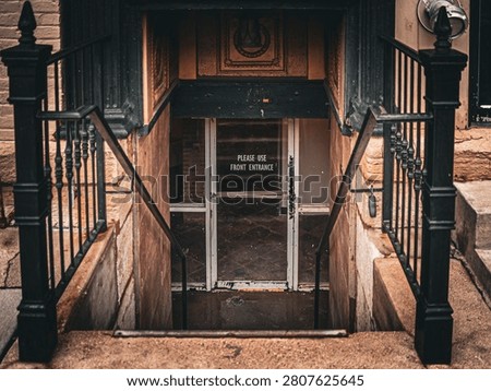 Symmetrical view looking down stone stairs toward a basement glass door with a notice reading please use front entrance between black iron railings
