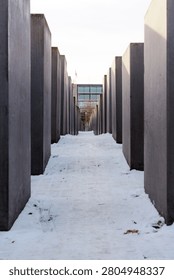Symmetrical view of a snowy path between concrete blocks at the Memorial to the Murdered Jews of Europe in Berlin, Germany.