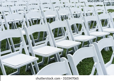 Symmetry of love: Rows of white folding chairs on lawn before a wedding ceremony in summer