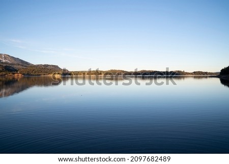 Symmetry in nature. View of the calm lake and shoreline in the horizon. The forest and clear blue sky reflection in the surface of the water. 