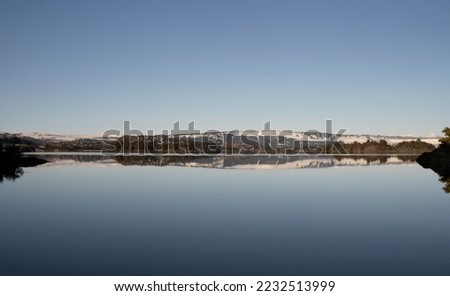 Symmetry in nature. View of the calm lake and shoreline in the horizon. The forest and clear blue sky reflection in the surface of the water.