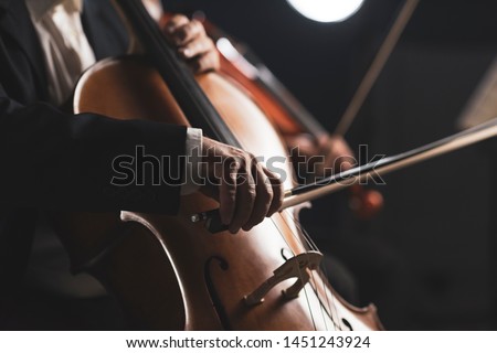 Symphonic orchestra performing on stage and playing a classical music concert, cellist in the foreground, hands close up
