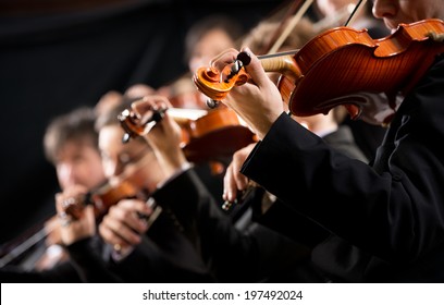 Symphony orchestra first violin section performing on dark background.