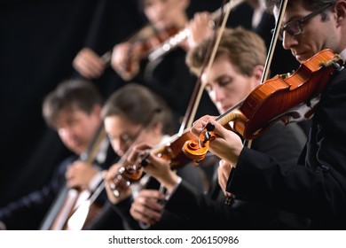 Symphony orchestra first violin section performing on dark background.