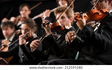 Symphony orchestra first violin section performing on dark background.