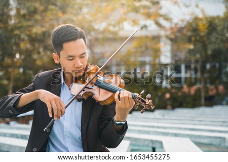 Symphony orchestra on outdoor background, hands playing violin. Male violinist playing classical music on violin. Talented violinist and classical music player solo performance.