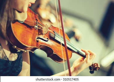 Symphony orchestra on stage, hands playing violin.
Shallow depth of field, vintage style.