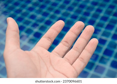 Symptom pruney and wrinkled skin hand and finger from water on blue pool swimming background at morning sunrise,Skin symptoms of hands and fingerprints,Healthy looking hands,Skin treatment. - Shutterstock ID 2370096601