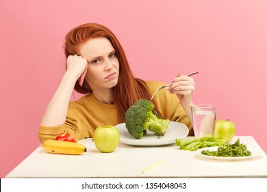 Symptoms Of Anorexia Manifested In Aversion To Food. Portrait Of Grimacing Unsatisfied Facial Emotional Expression Lady Refusing To Eat Fresh Green Salad In Bowl On Table In Light Room