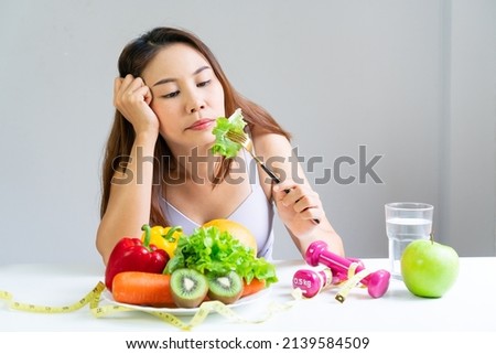 Symptoms of anorexia manifested in aversion to food. Portrait of young Asian woman in unsatisfied facial emotional expression, refusing to eat vetables and fruits. Close up