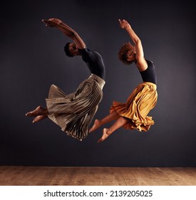 Synchronisity. Two Contemporary Dancers Performing A Synchronized Leap In Front Of A Dark Background.