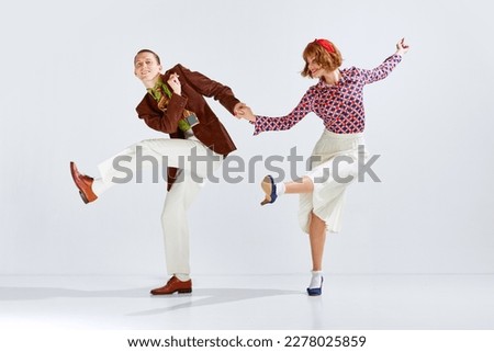 Synchronization of movements. Yung positive man and woman in stylish clothes dancing retro dance against grey studio background. Concept of art, retro style, hobby, party, movements, 60s, 70s culture