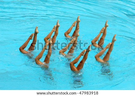 Synchronized Swimmers point up out of the water in action