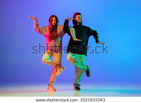 Synchronous movements. Two young people, guy and girl, dancing contemporary dance, hip-hop over blue background in neon light. Youth culture, modern dance aesthetics concept