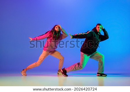 Synchronous movements. Two young people, guy and girl, dancing contemporary dance, hip-hop over blue background in neon light. Youth culture, modern dance aesthetics concept
