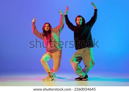 Synchronous movements. Two young people, guy and girl, dancing contemporary dance, hip-hop over blue background in neon light. Modern dance aesthetics concept