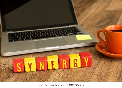 Synergy written on a wooden cube in front of a laptop