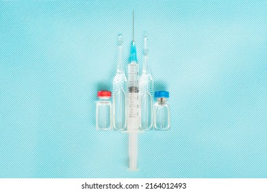 Syringe in the center of scene and red and blue ampoules with vaccine against virus situated vertical on blue background. Copy space.