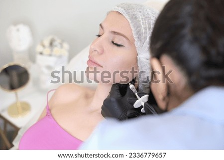 With syringe in hand, beauty doctor is shown performing injection into the patient's jowls, part of effective treatment sculpt facial contour. patient lying during non-surgical face lift procedure