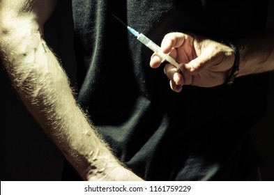 syringe in hand on a dark background - Shutterstock ID 1161759229