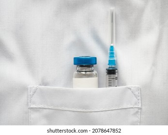 Syringe And Injection Vial Lying In The Pocket Of A Doctor's Gown. Close-up, Indoors, No People. Daylight, Studio Photo. Healthcare Concept