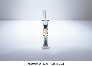 A syringe of marijuana distillate for refillable vaporizer cartridges.  On white surface with white background, spot light, with gradients.  Close up isolated shot.