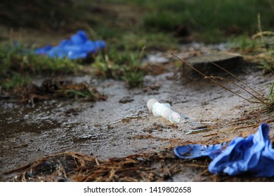 Syringe And The Needle In The Mud On The Ground With Medical Gloves Around.