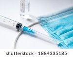 Syringe with needle, vial and surgical face mask on a white table ready to be used. Covid or Coronavirus vaccine or monoclonal antibodies background