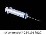 A syringe is shown on a black background. The syringe is clear and has a black rubber stopper