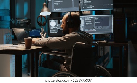 System admin using terminal window on laptop to program new code, dealing with physical impairment. Male web developer in wheelchair coding firewall security or html script. Tripod shot.