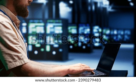 System administator using laptop to audit server mainframes with high computing power, enabling high tech facility to support demanding applications such as machine learning and 3D rendering workloads