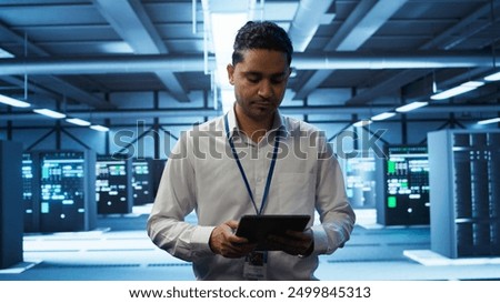 System administrator in data center managing and maintaining databases, ensuring data integrity, security and availability. IT worker updating server room supercomputers systems, camera B