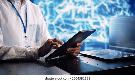System administrator in data center, solving tasks on tablet while running programming scripts on laptop terminal. Experienced programmer manipulating lines of code for AI applications development