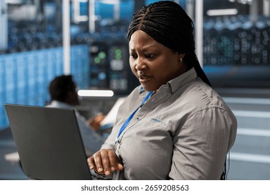 System administrator in server room using laptop to implement and manage data backup solutions. Data center IT expert identifying and resolving technical errors, ensuring efficient recovery
